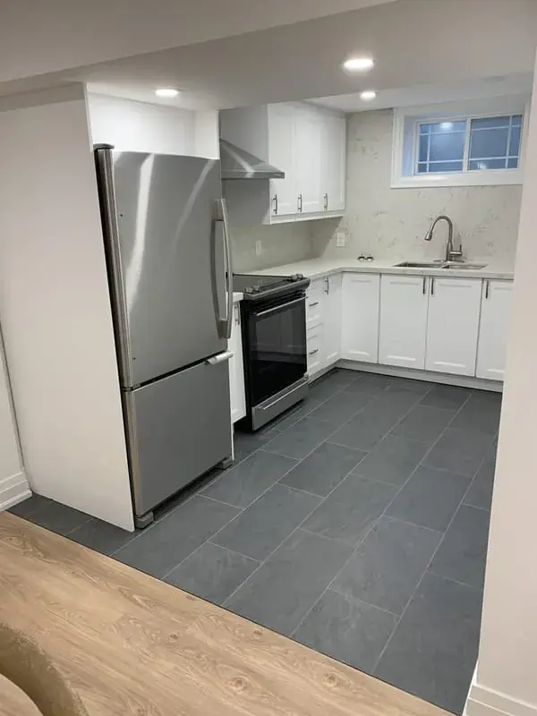 Basement kitchen with white cabinets, a grey tile floor and a small window