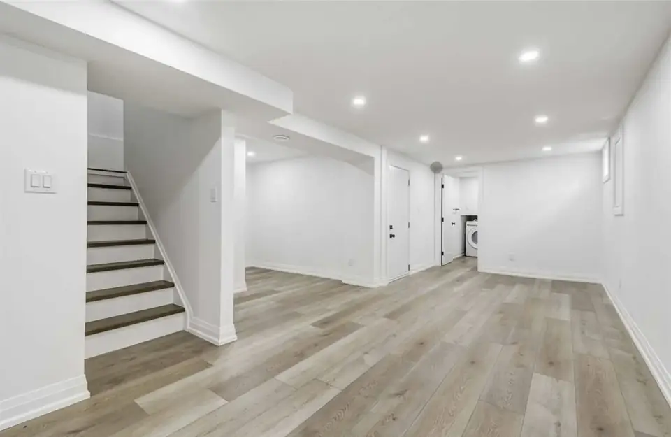 Finished basement with vinyl plank floor, pot lights, white walls and an open stair