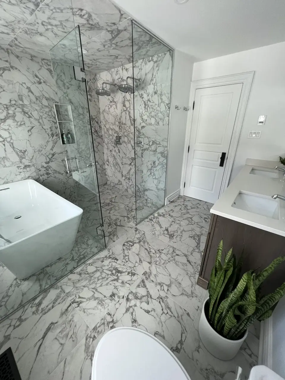 Bathroom: marble-look tile, glass shower, white vanity and toilet