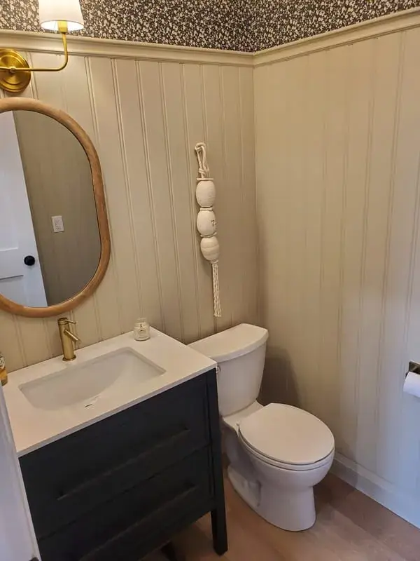Small powder room with beadboard, patterned wallpaper and an oval mirror