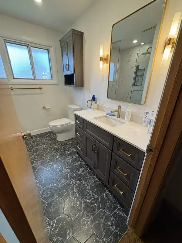 Dark vanity with gold fixtures over a black hex tile floor