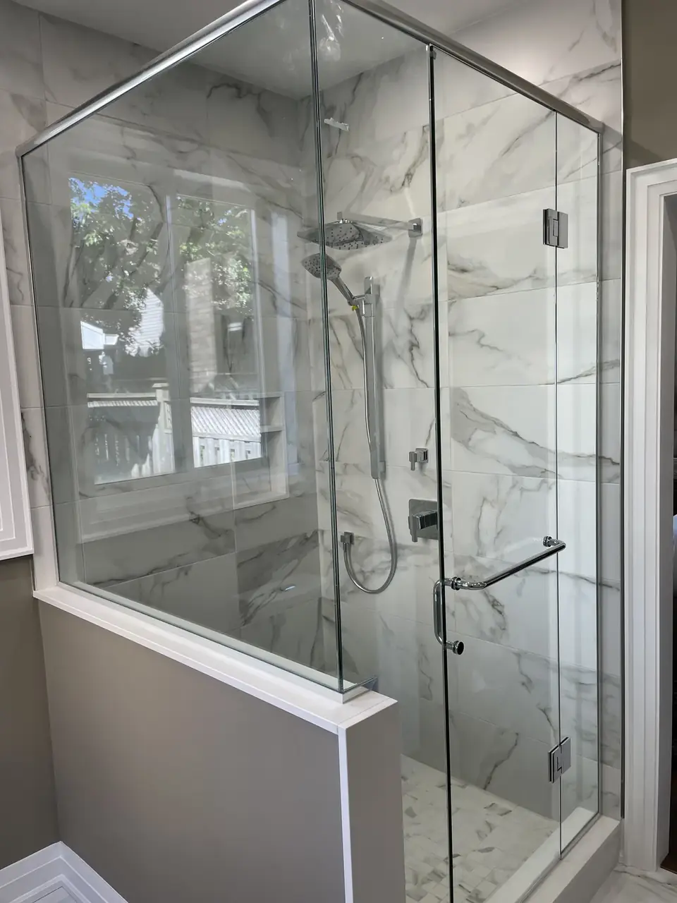 Frameless glass shower with marble-look tile and a rain head