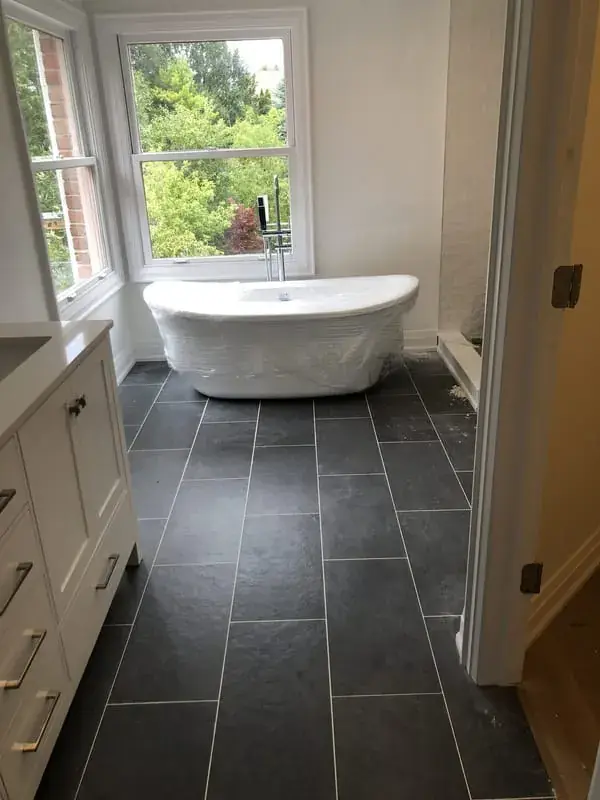 Freestanding tub under a window on a dark tile floor