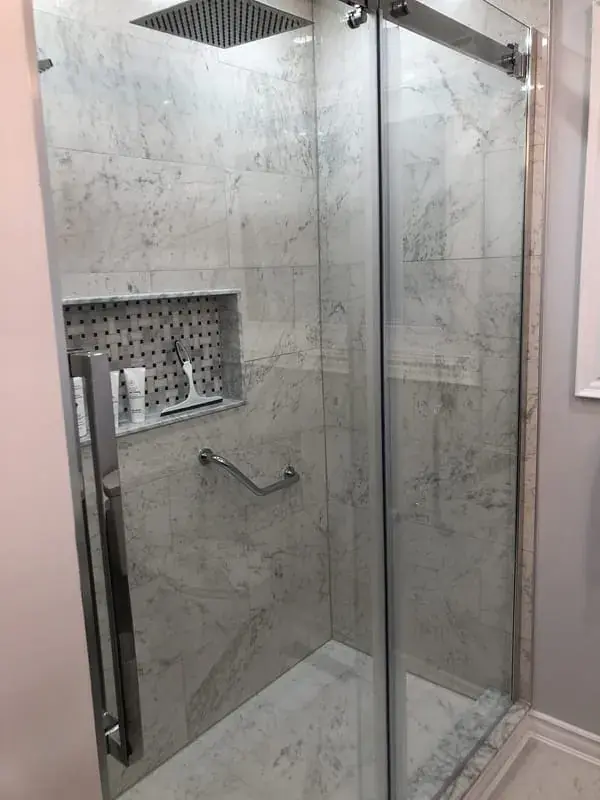 Marble-look walk-in shower with a glass door and a built-in wall niche
