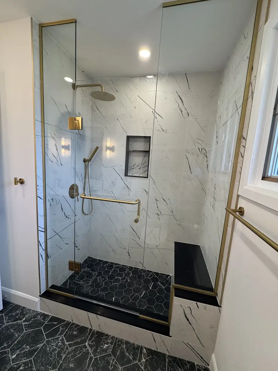 Walk-in shower, marble tile, glass, gold fixtures, black mosaic floor and bench