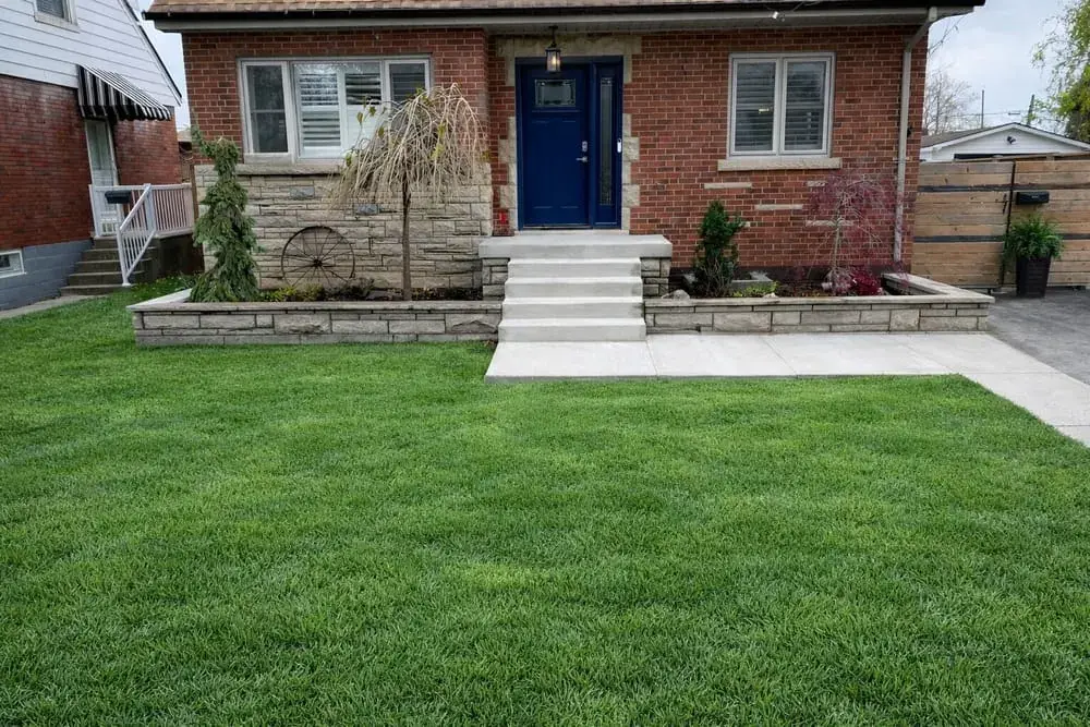 Brick bungalow with wide stone steps, planter walls and a navy door