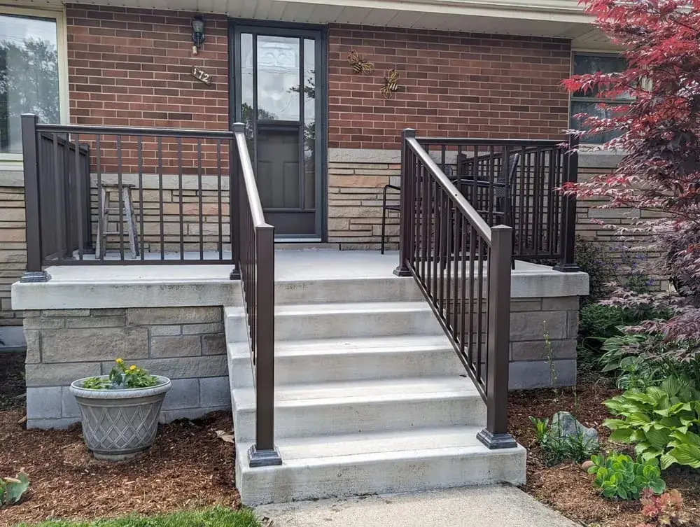 Brick home with wide concrete steps, dark metal railings and stone side walls