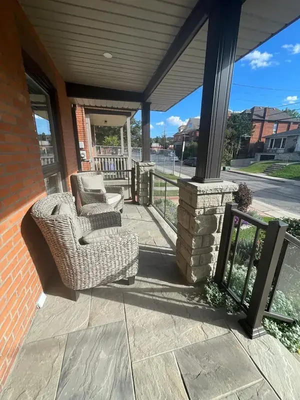 Covered porch with wicker chairs beside a stone column on a flagstone floor