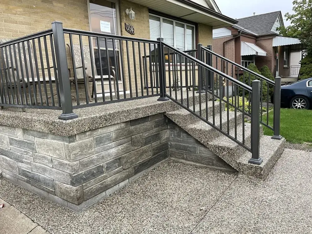 Exposed aggregate porch with stone skirting and a black railing