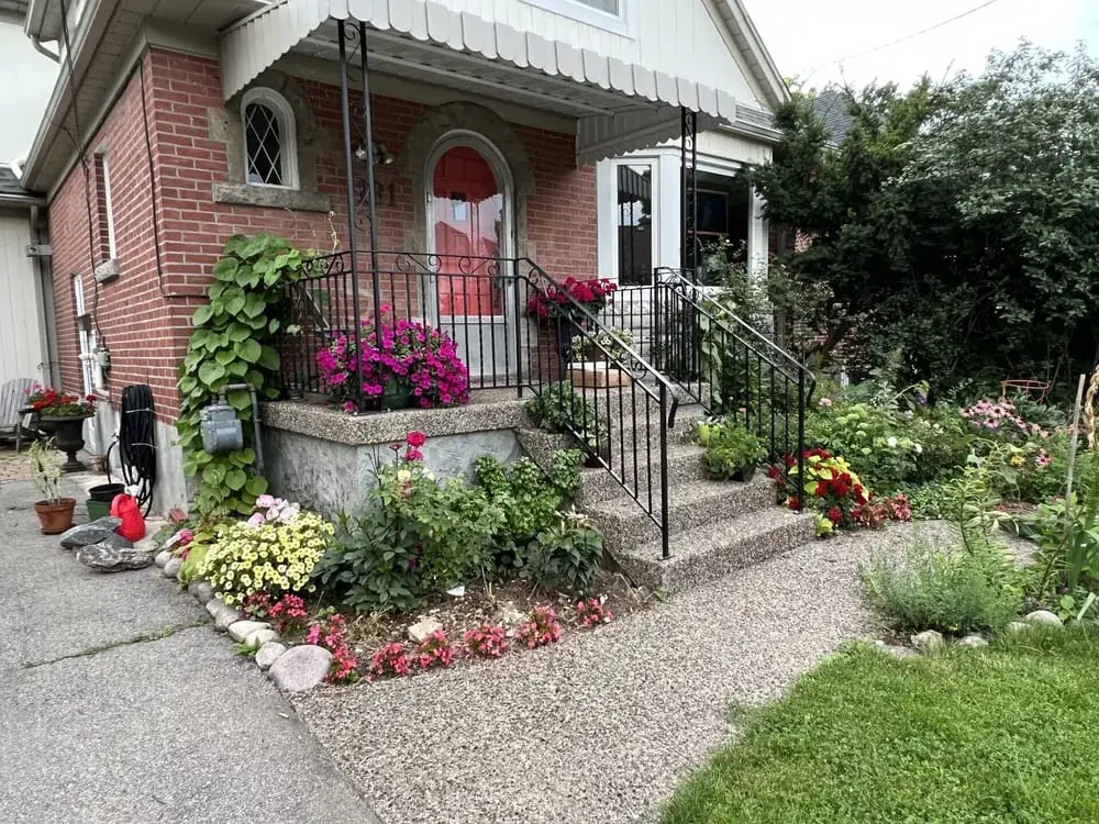 Exposed aggregate steps with iron railings beside a dense flower garden