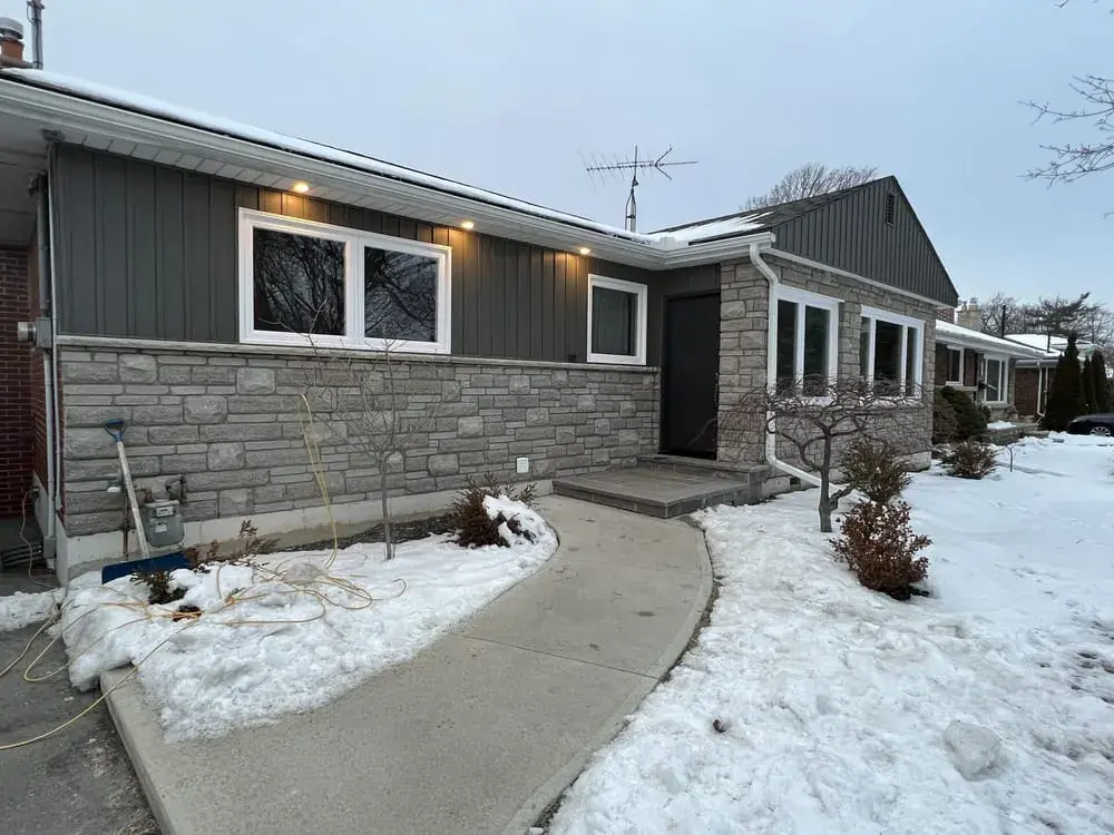 The re-clad bungalow in winter, snow on the lawn and a curved walk to the door
