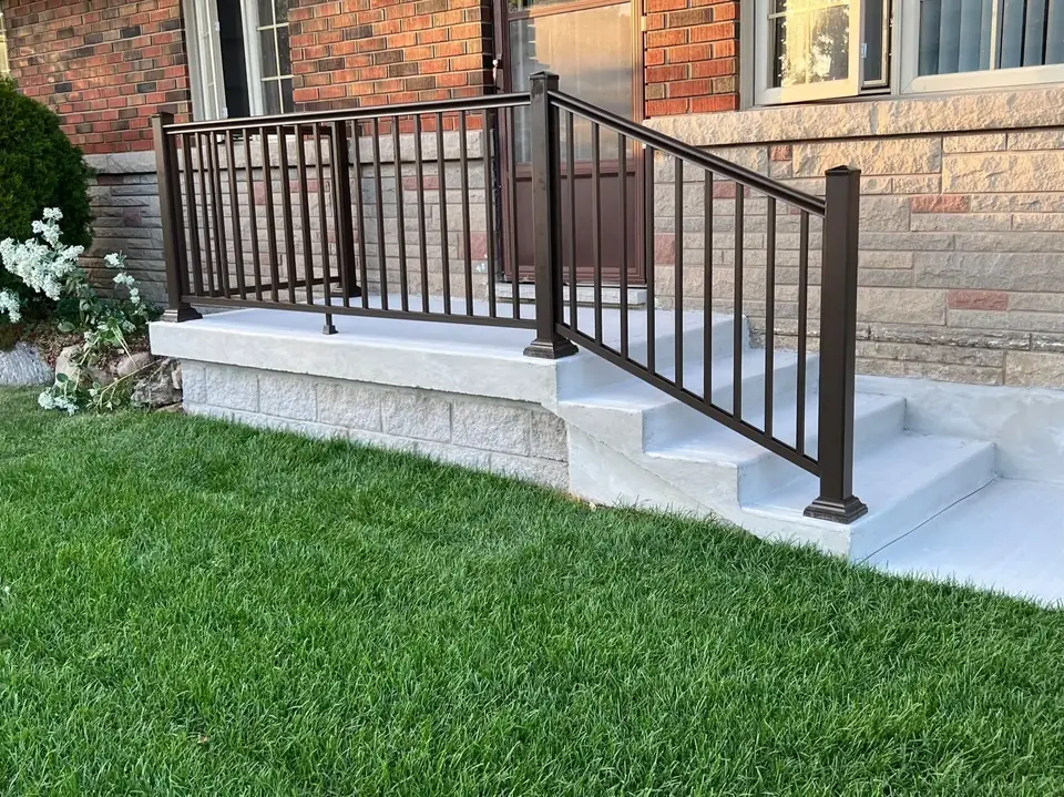 Light stone clad front porch and steps with a black railing on a red brick house