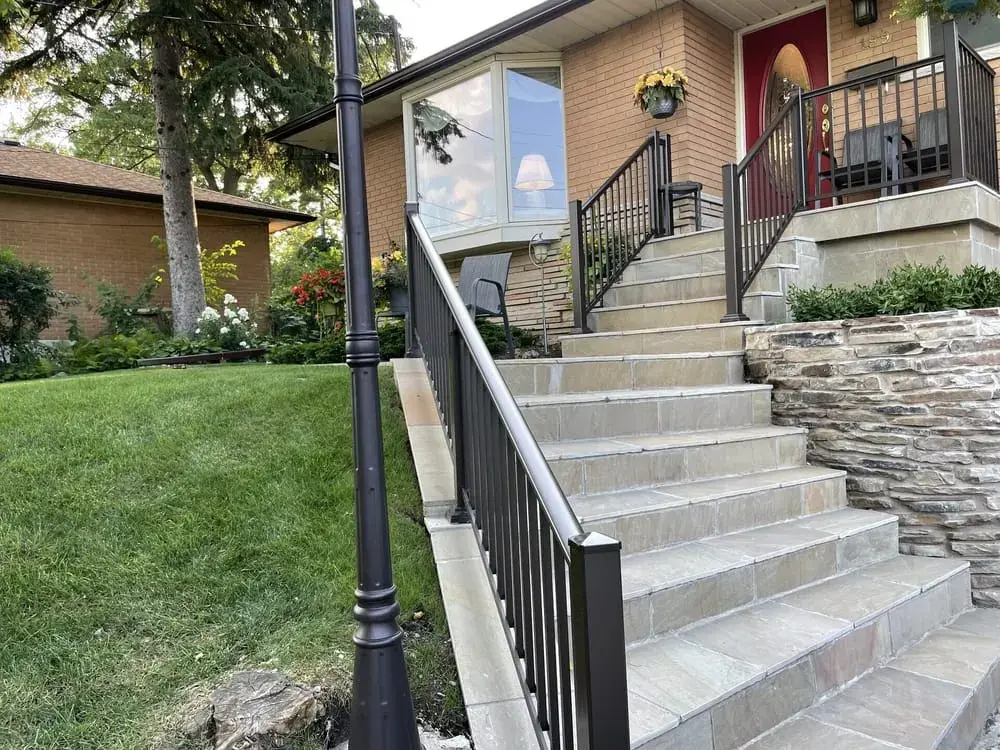 Long stone staircase with a stacked-stone wall and black railing up a slope