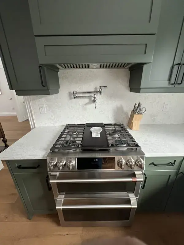 Gas range with a pot filler under a panelled hood, green cabinets
